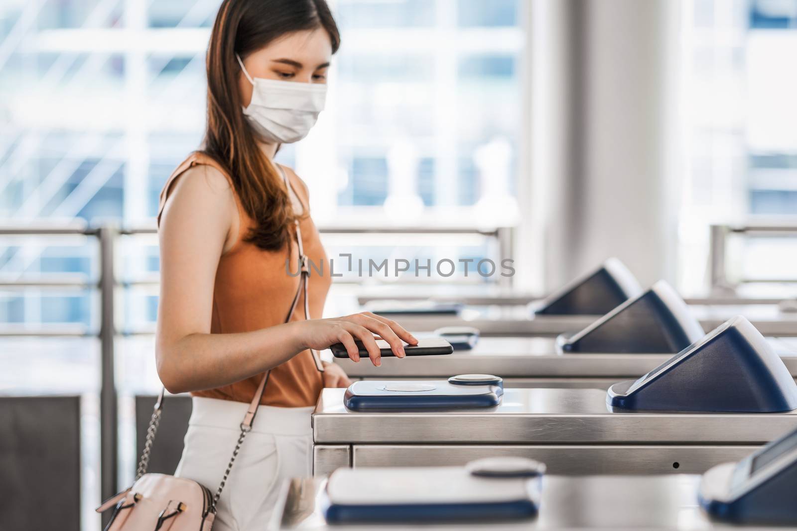 Closeup hand using smart mobile phone of Young Asian woman passenger wearing surgical mask for scanning the automatic machine by QR code to subway or bus station when traveling in big city