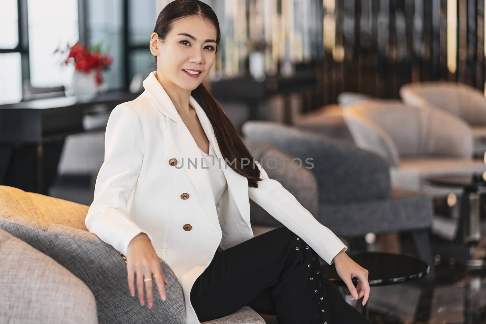 Portrait Asian businesswoman wearing formal suit sitting on the sofa in modern lobby, office or coworking space, coffee break leisure, fashion and lifestyle after working time,business people concept