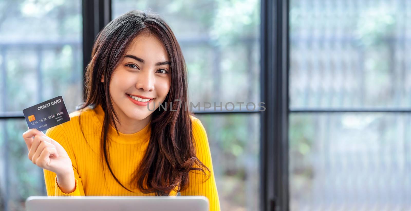 Young Asian woman presenting credit card for online shopping in coffee shop or coworking space,technology money wallet and online payment concept,copy space for banner or cover page credit card mockup