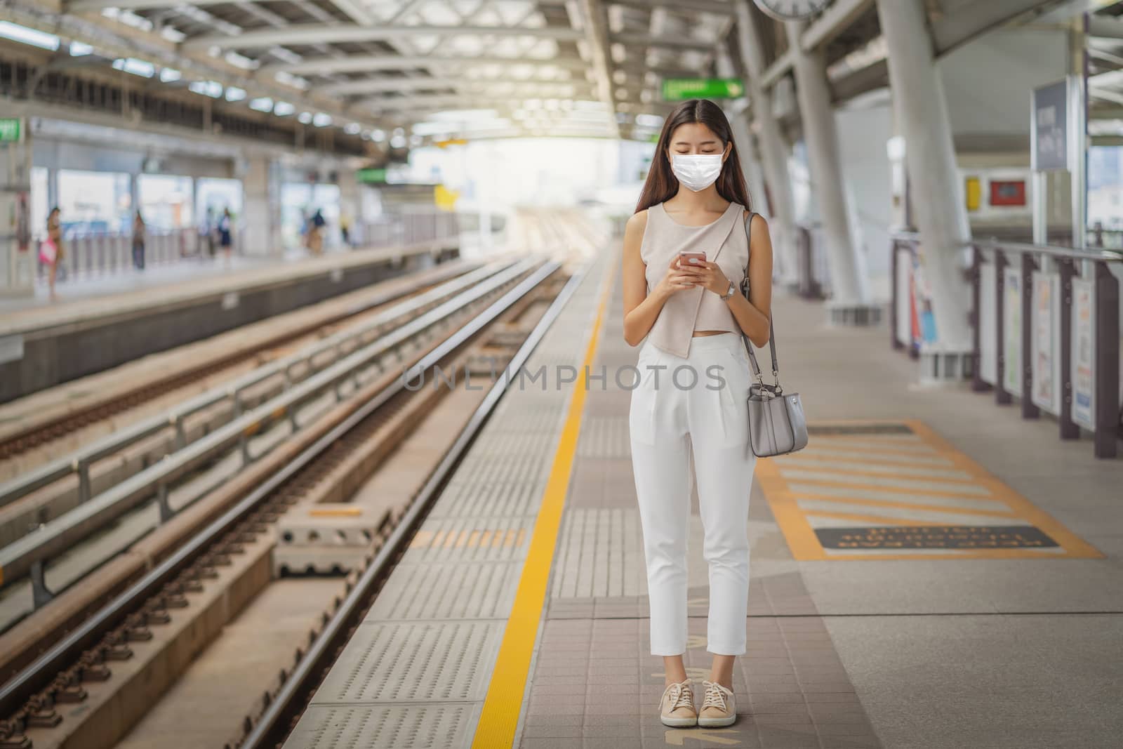 Young Asian woman passenger wearing surgical mask and using social network via smart mobile phone in subway train when traveling in big city, commuter and transportation with covid-19 outbreak concept