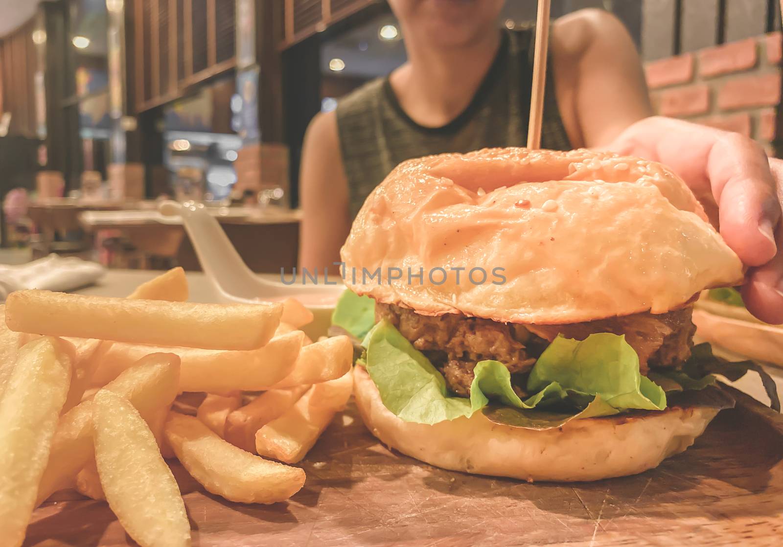 Woman trying to pick up hamburger and french fries on the wood table.Junk food and cholesterol. Close up and blur.