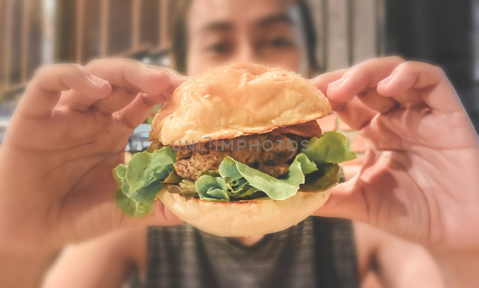 Woman pick up hamburger in two hands.Junk food and cholesterol. Close up and blur.