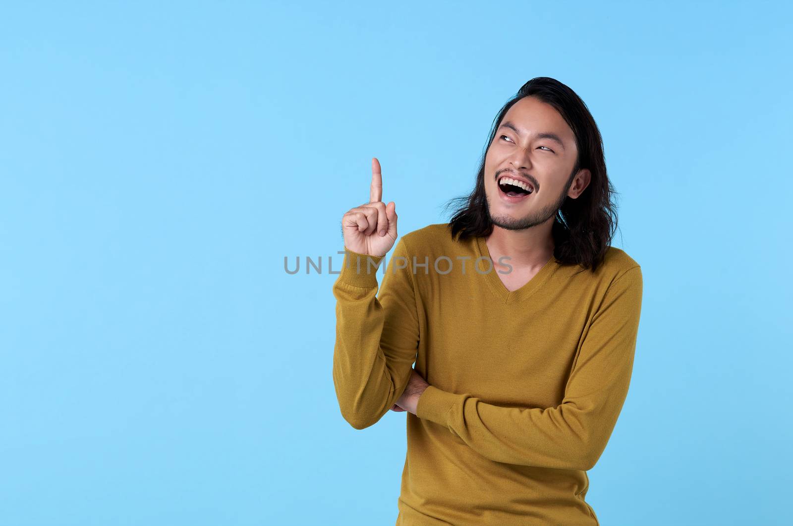 Wow and surprised young Asian man smiling with his finger pointing on blue background with copy space. by barameeyay