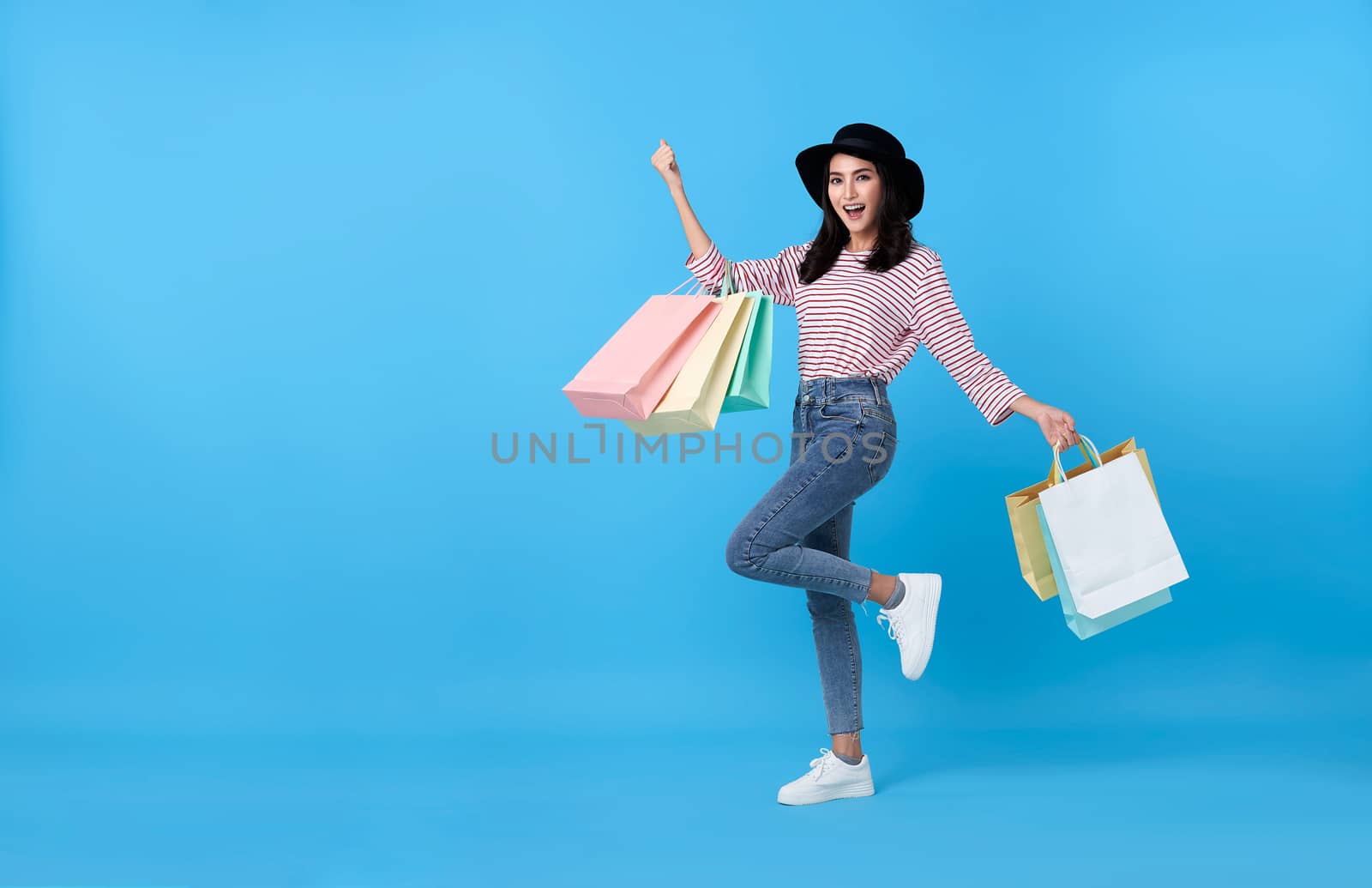 Happy young thai asian female carrying with both arms raised in a ecstatic gesture and shopping bags on blue copy space background. by barameeyay