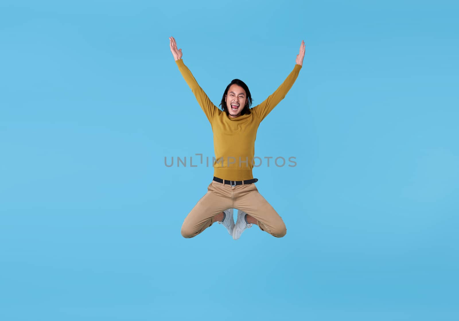 Happy energetic young Asian man jumping in mid-air isolated on blue background. by barameeyay