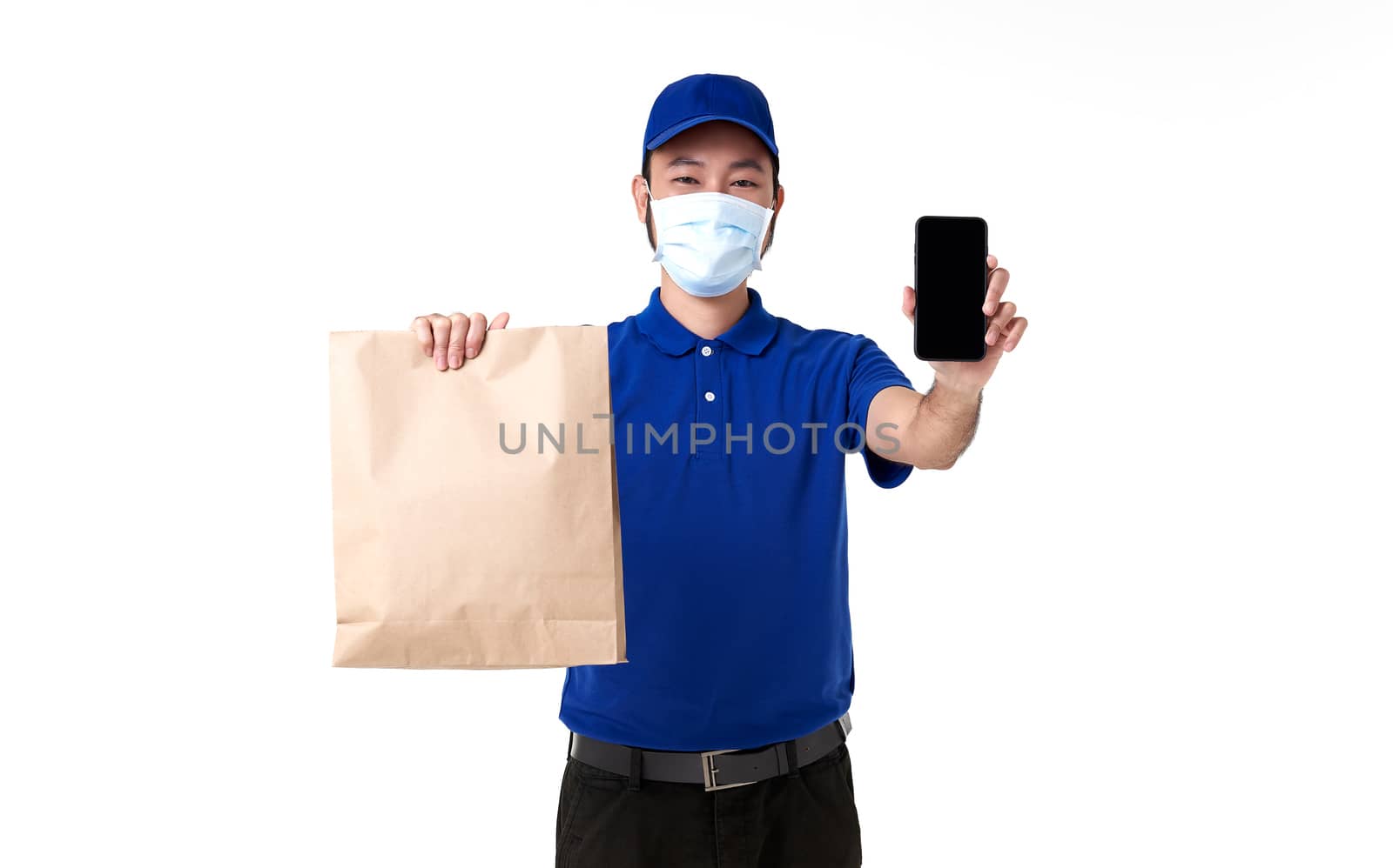 Asian delivery man wearing face mask in blue uniform with smart phone holding paper bag isolated on white background. express delivery service during covid19.