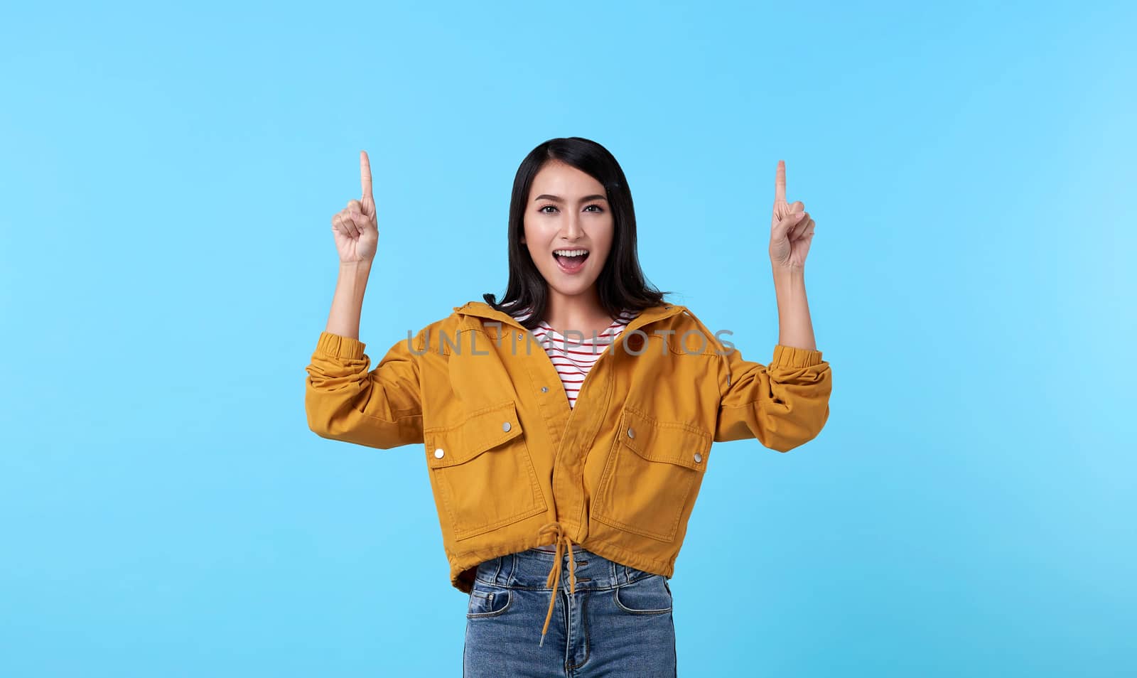 Smiling happy asian woman with her finger pointing isolated on light blue banner background with copy space.