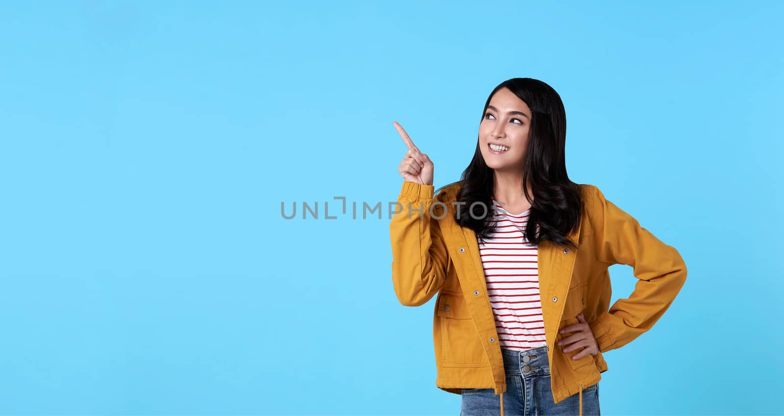 Smiling happy asian woman with her finger pointing isolated on light blue banner background with copy space. by barameeyay
