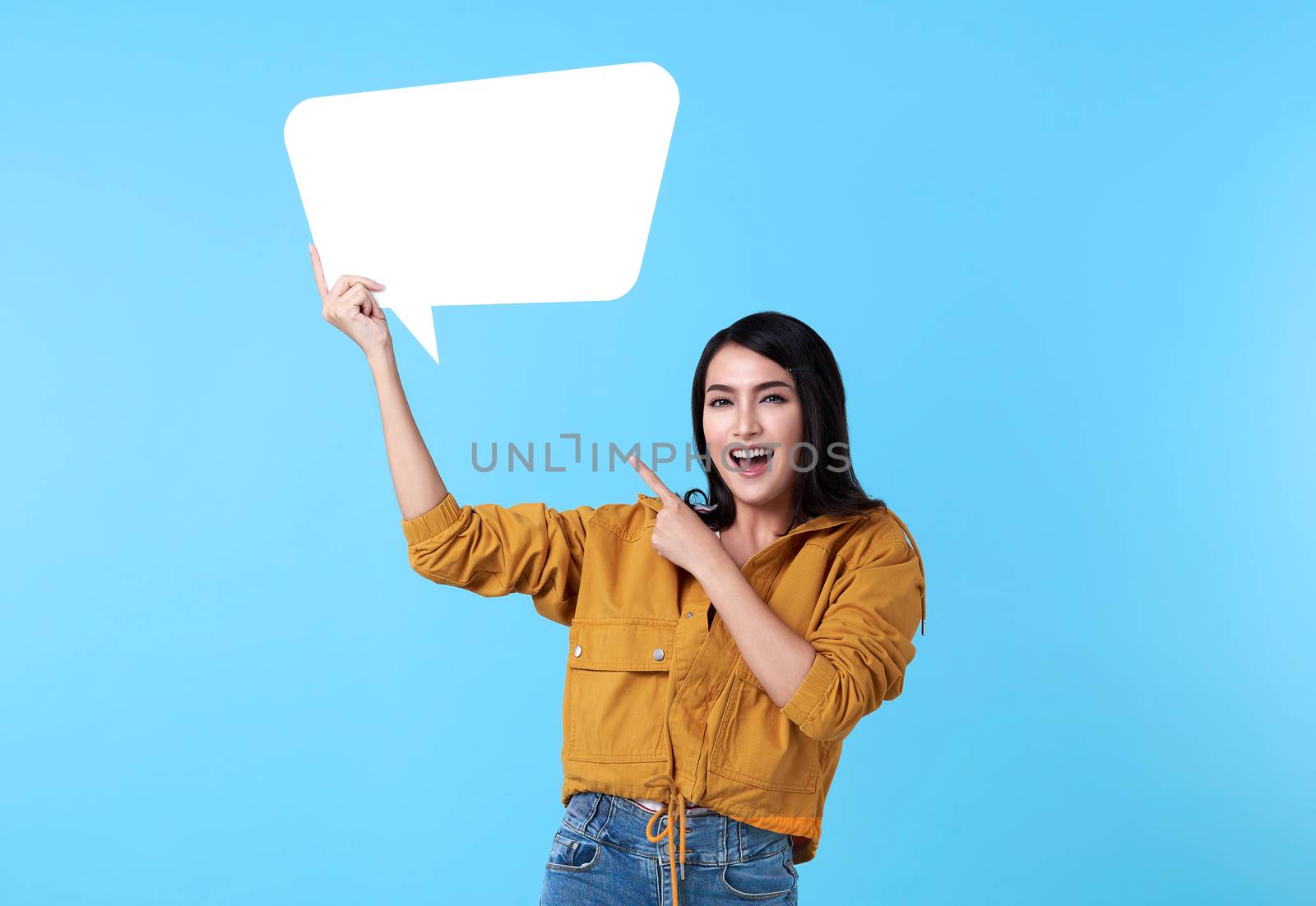 Smiling happy asian woman holding blank speech bubble and with empty space for text on blue background.