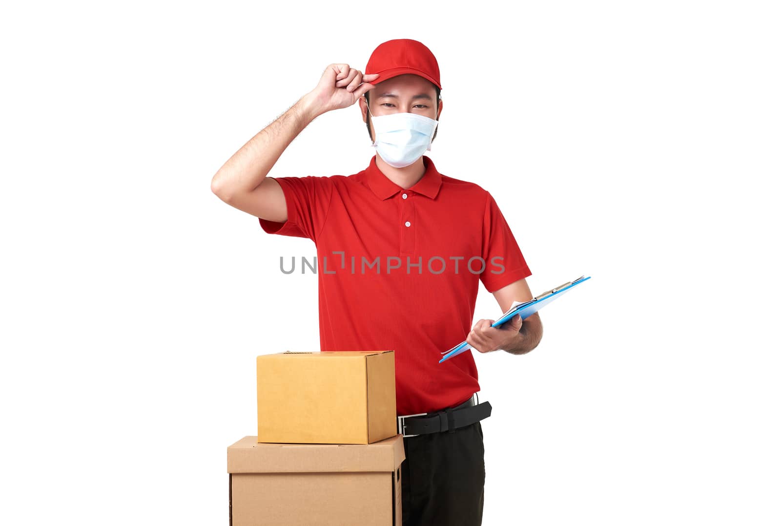 Asian delivery man wearing face mask in red uniform standing with parcel post box isolated over white background. express delivery service during covid19. by barameeyay