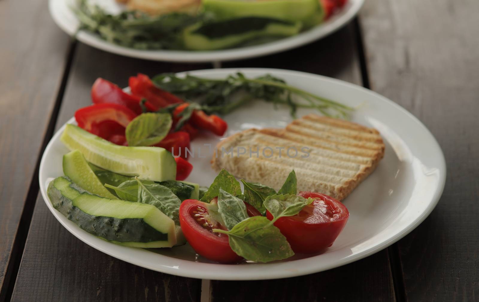 Healthy organic vegetable breakfast, tomato, toast, salad, basil, cucumber, arugula. Vegetarian healthy food in a white plate on a dark wooden table. High quality photo