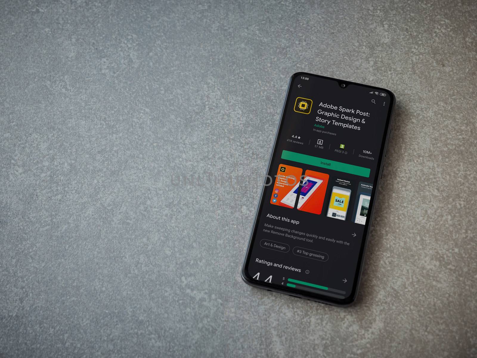 Lod, Israel - July 8, 2020: Adobe Spark Post - Graphic Design and Story Templates app play store page on the display of a black mobile smartphone on ceramic stone background.Top view flat lay with copy space
