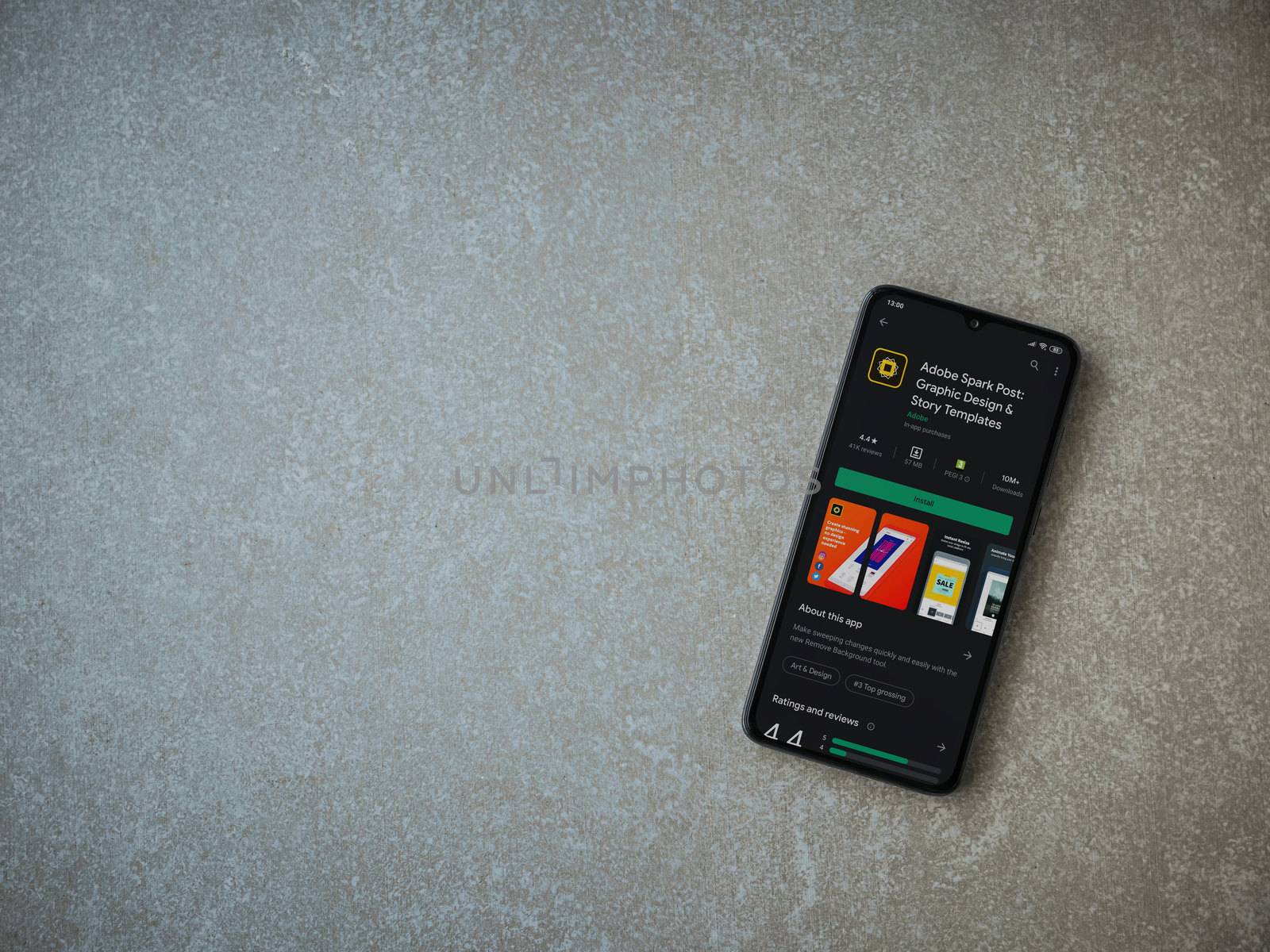 Lod, Israel - July 8, 2020: Adobe Spark Post - Graphic Design and Story Templates app play store page on the display of a black mobile smartphone on ceramic stone background.Top view flat lay with copy space