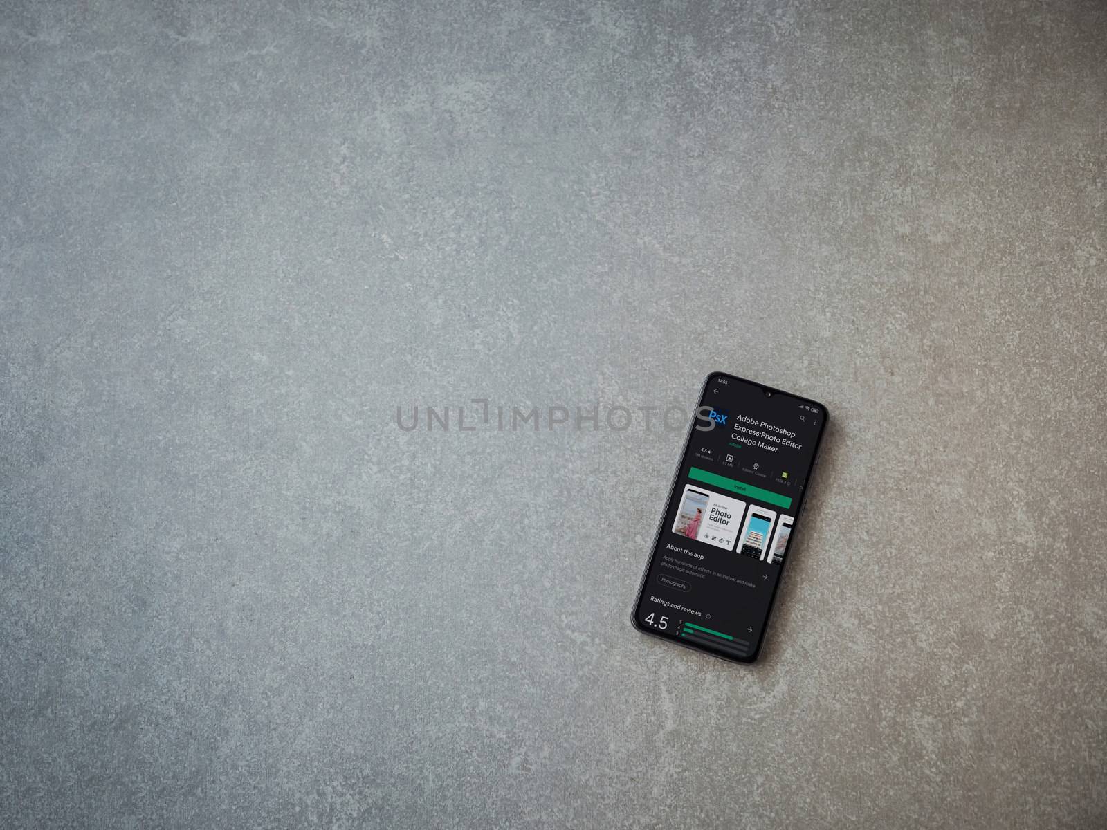 Lod, Israel - July 8, 2020: Adobe Photoshop Express Photo Editor app play store page on the display of a black mobile smartphone on ceramic stone background. Top view flat lay with copy space.
