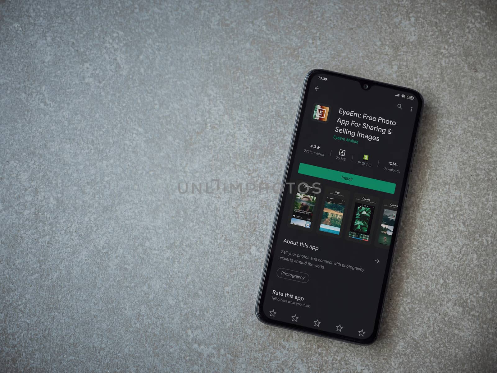 Lod, Israel - July 8, 2020: EyeEm - Sharing and Selling Images app play store page on the display of a black mobile smartphone on ceramic stone background. Top view flat lay with copy space.