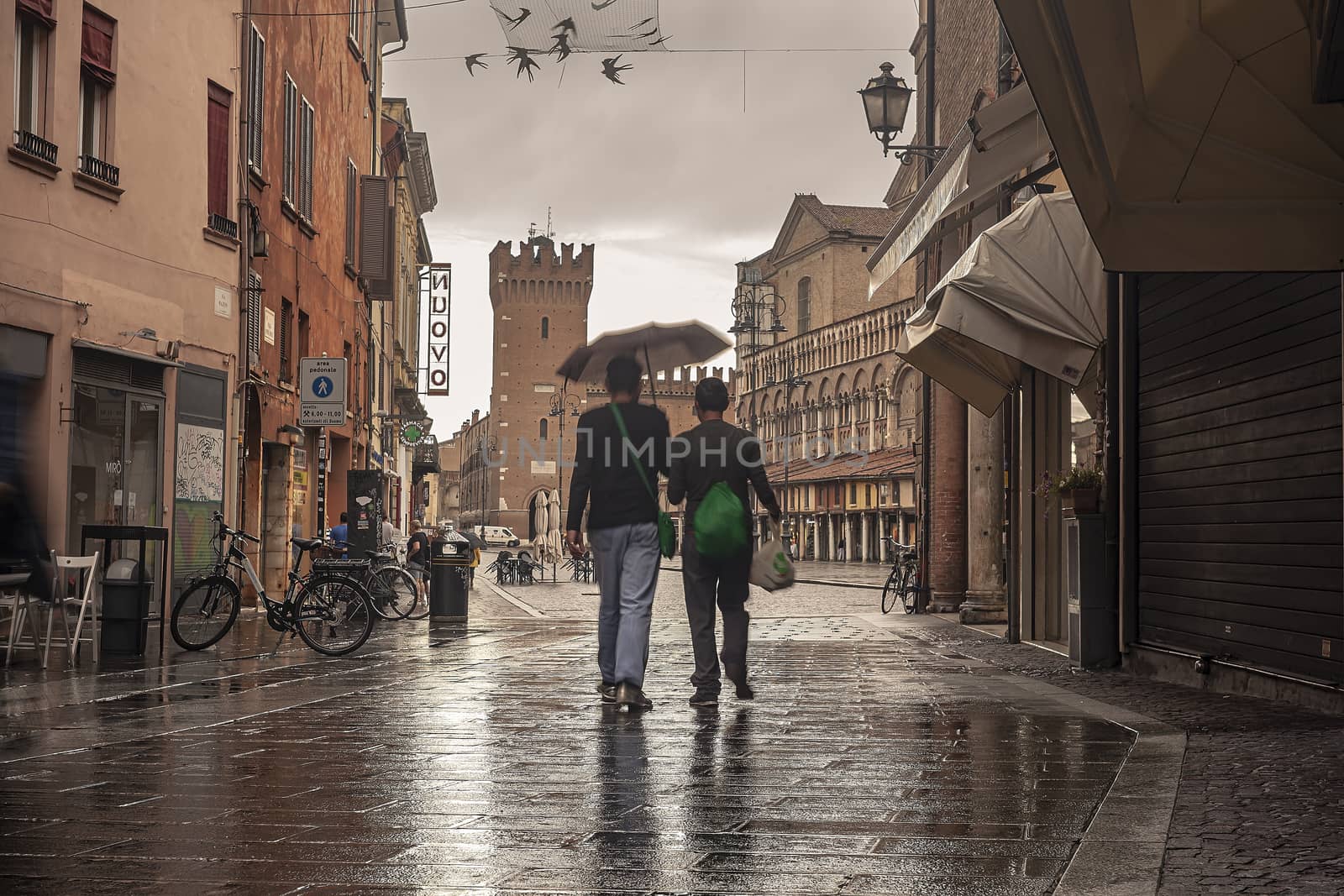 FERRARA, ITALY 29 JULY 2020 : Evocative view of the street that leads to Piazza Trento Trieste in Ferrara in Italy with people in their daily lives