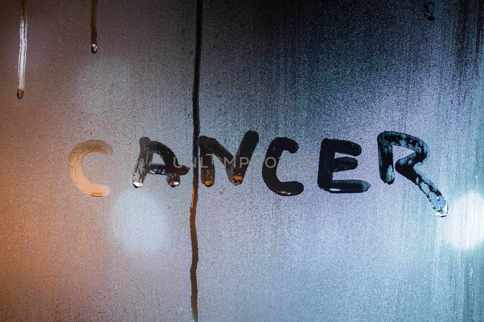 the word cancer written by finger on night wet glass with blurred sttreet light in background.