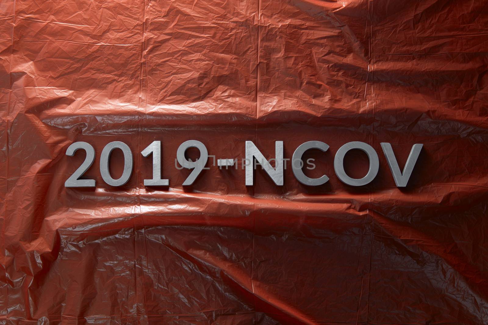 The word 2019-NCOV laid with metal letters on crumpled red plastic film background in flat lay centered composition and dramatic light. Abstract chinese coronavirus concept,