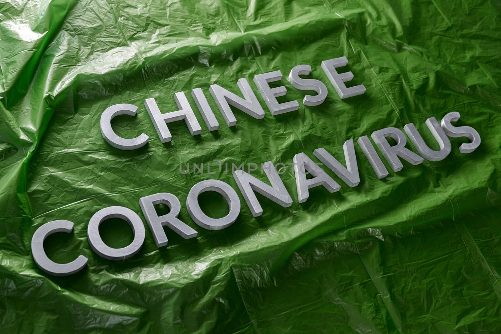 The words chinese coronavirus laid with silver metal letters on green crumpled plastic film with diagonal perspective and selective focus. Pandemic flu concept.