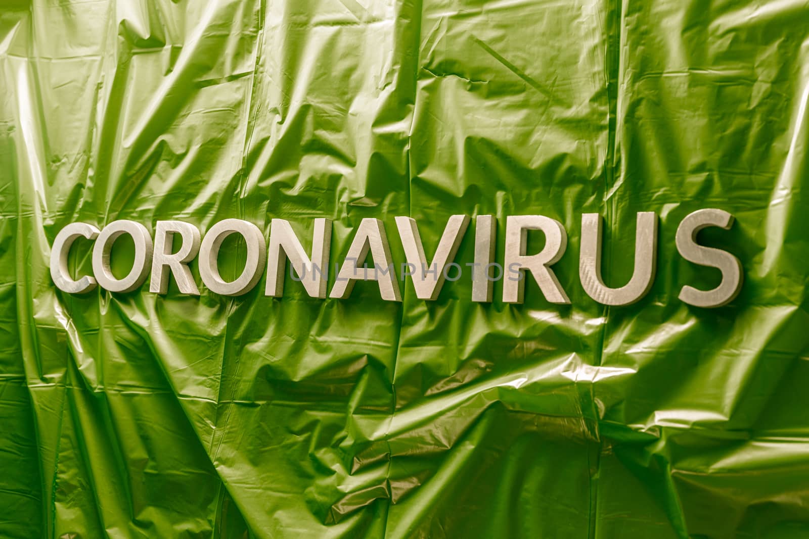 word coronavirus laid with silver letters on crumpled green plastic coat - in perstpective view with selective focus and dramatic cold light