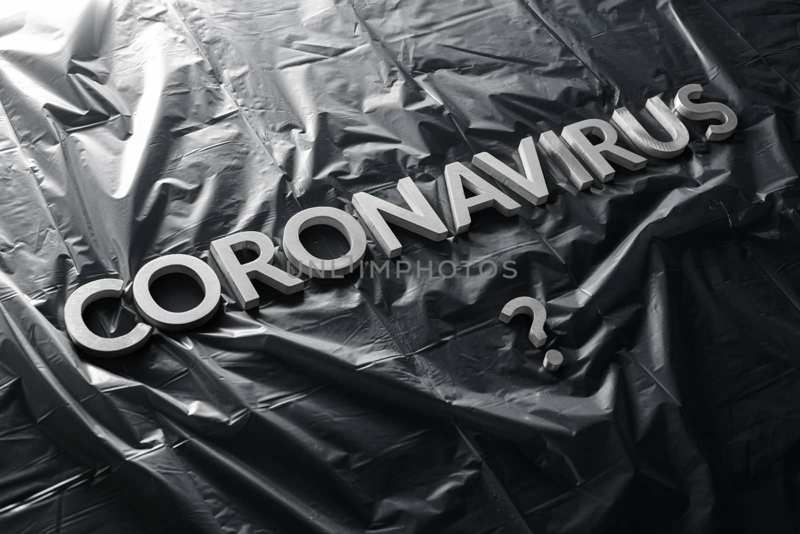 a question coronavirus laid with silver letters on black crumpled blue plastic film - diagonal composition with selective focus and dramatic light