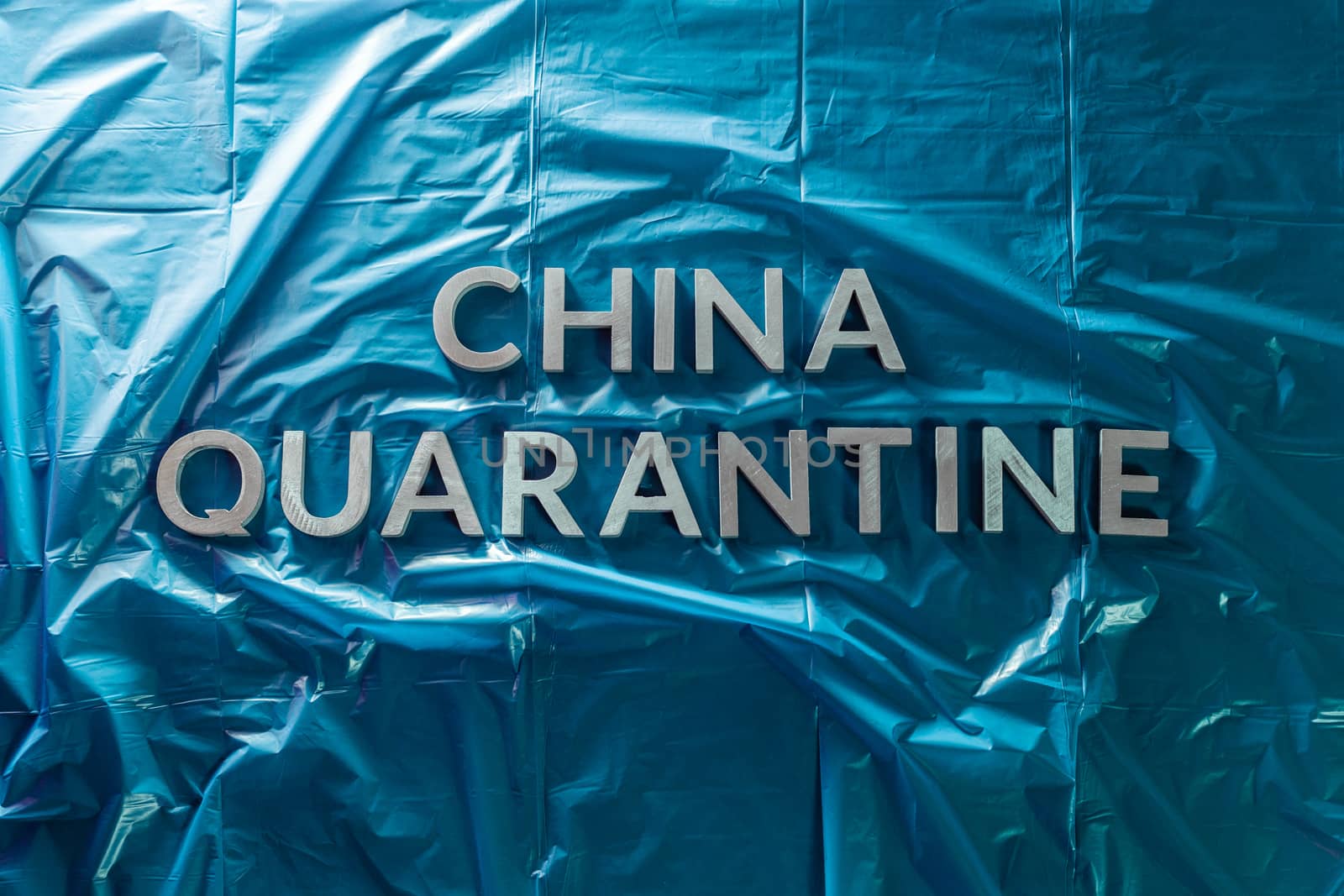 the words china quarantine laid with brushed silver metal letters on crumpled blue plastic film in flat lay straight perspective and dramatic light