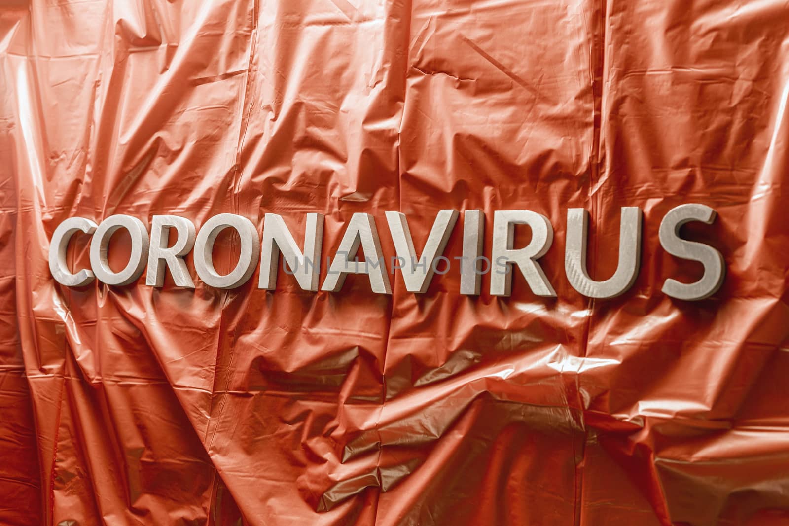 word coronavirus laid with silver letters on crumpled blue plastic coat - in perstpective view with selective focus and dramatic cold light