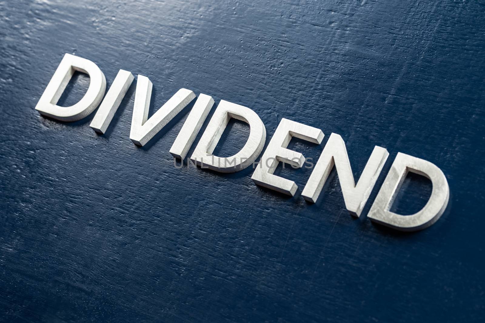 the word dividend laid by silver metal letters on gloss painted board background with selective focus in diagonal perspective