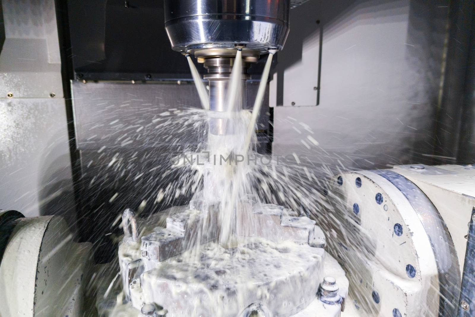 a process of industrial wet milling in 5-axis cnc machine with coolant flow under pressure and motion blur of streams and splashes.