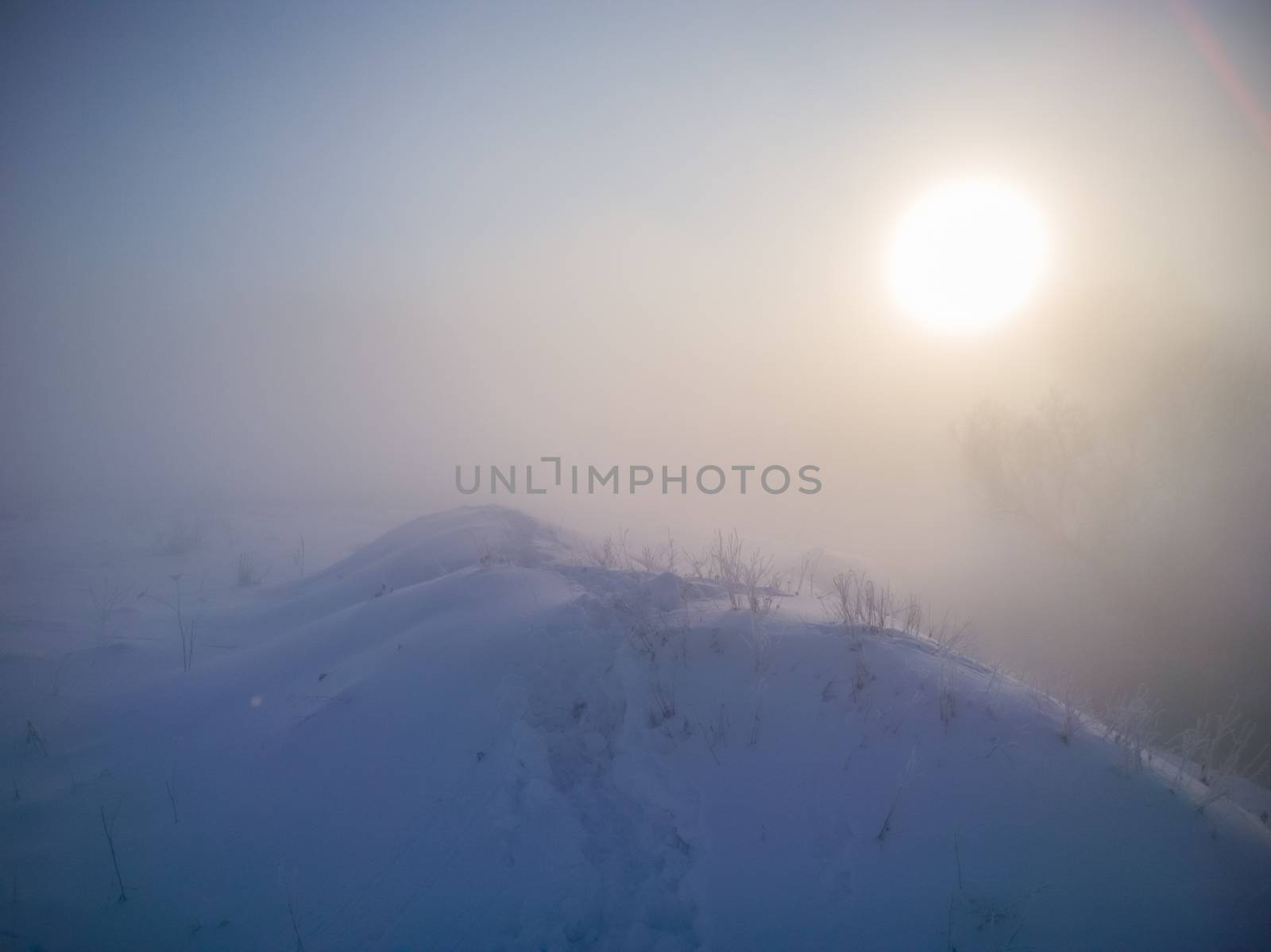 winter snow hill with footprints in deep snow at foggy morning.