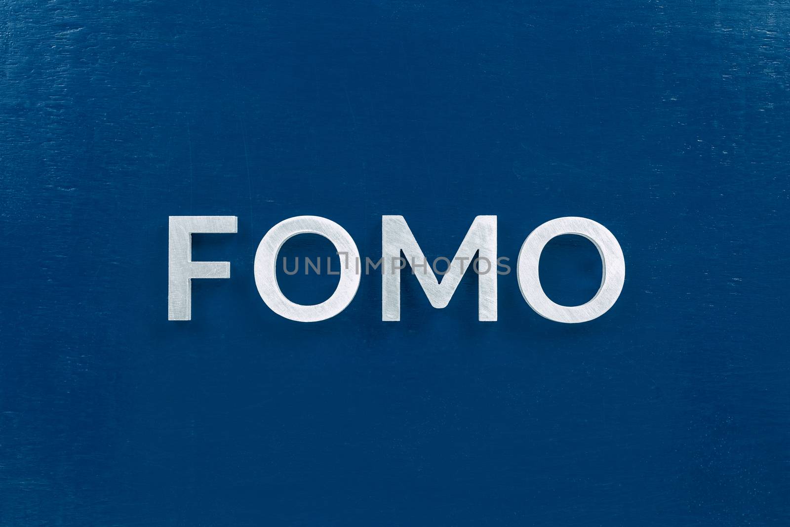 The abbreviation word fomo - fear of missing out - laid with silver letters on classic blue color flat painted surface. Stock market or crypto trading concept.