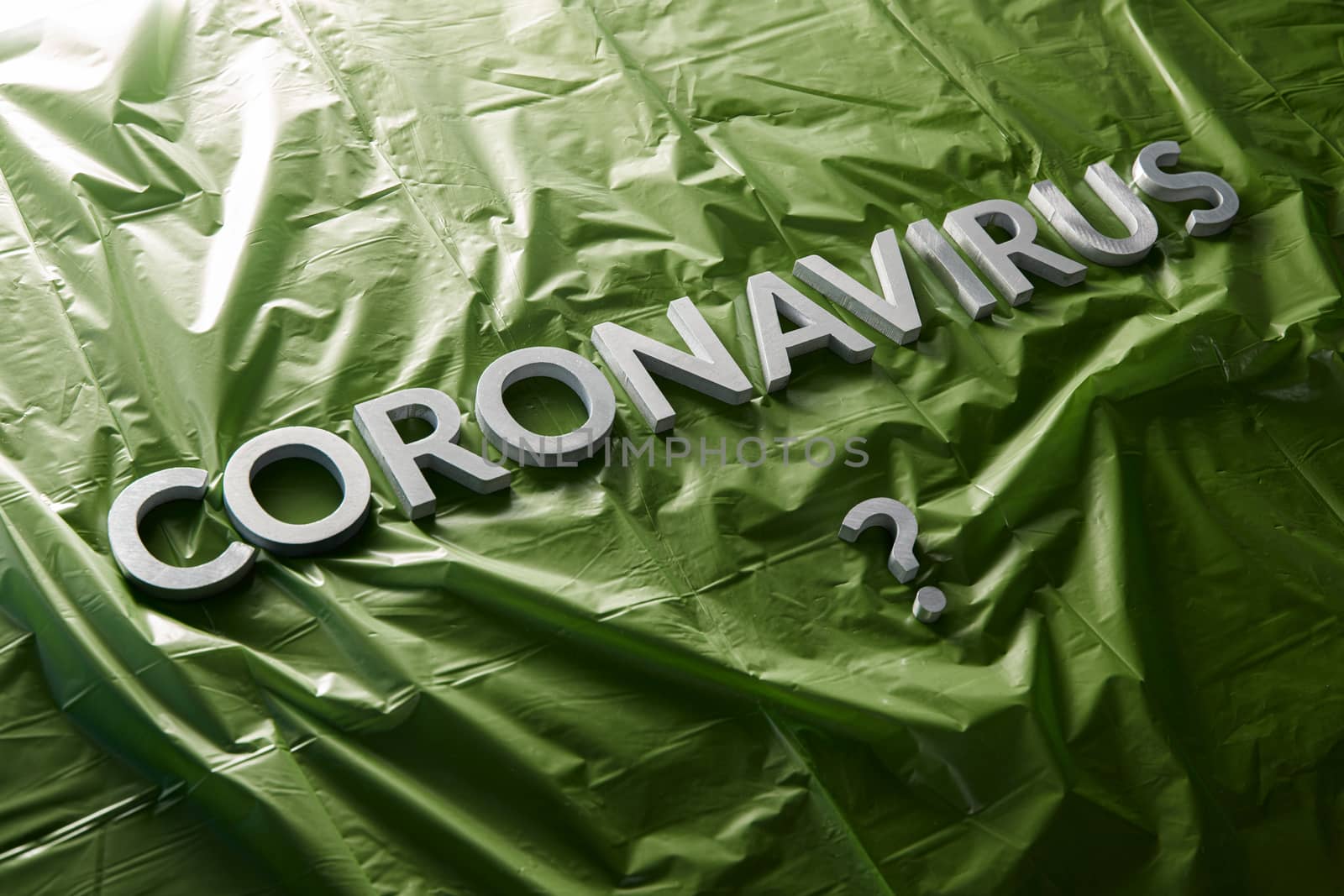 a question coronavirus laid with silver letters on crumpled green plastic film - diagonal composition with selective focus and dramatic light