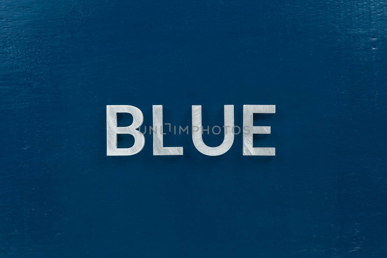 the word blue laid with silver metal letters on classic blue painted board background.