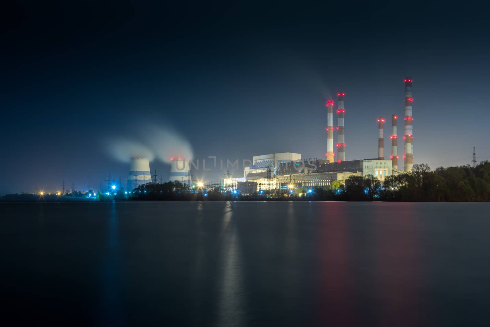 old thermal 450 megawatt power plant at night with artificial lake on foreground.