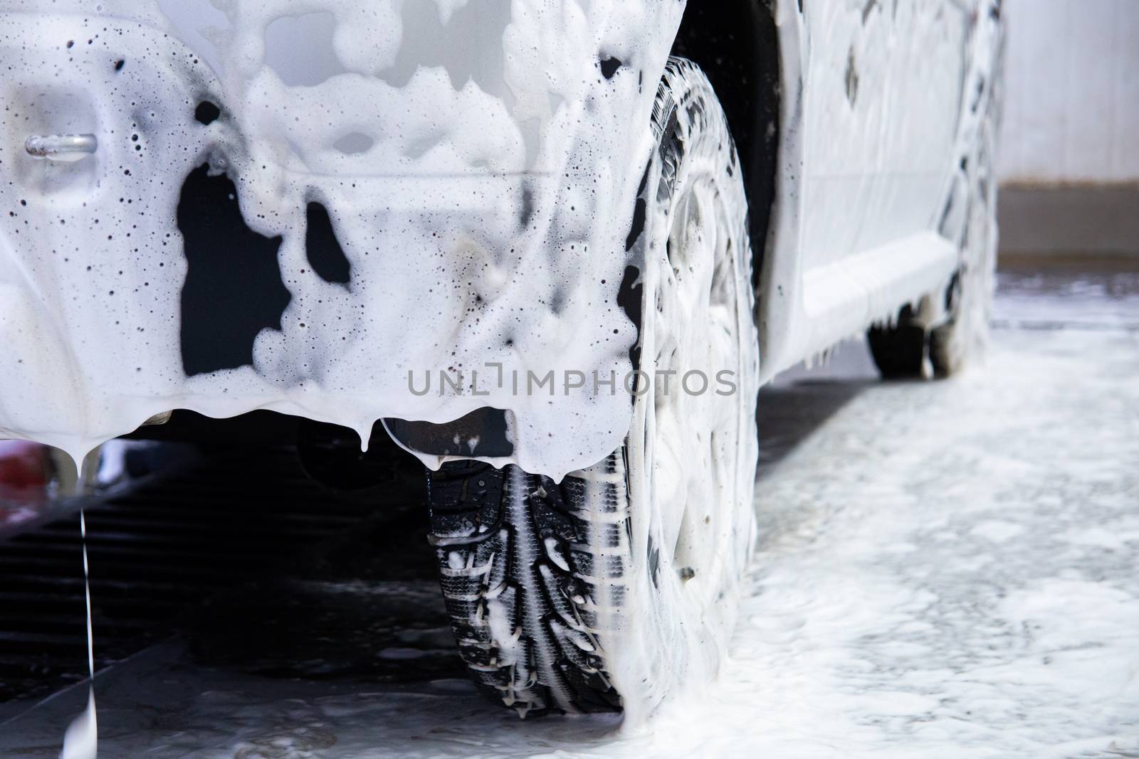 a car covered by soap foam while washing indoors - close-up low position view from back with selective focus.