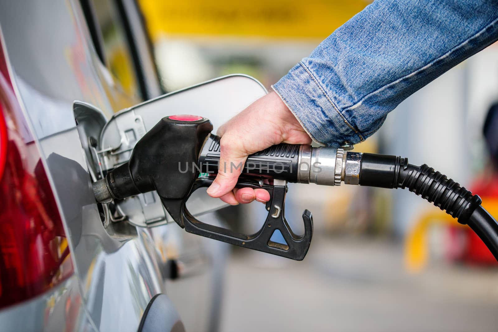hand in jeans jacket refueling gray metallic car on gas station - closeup with selective focus and blur