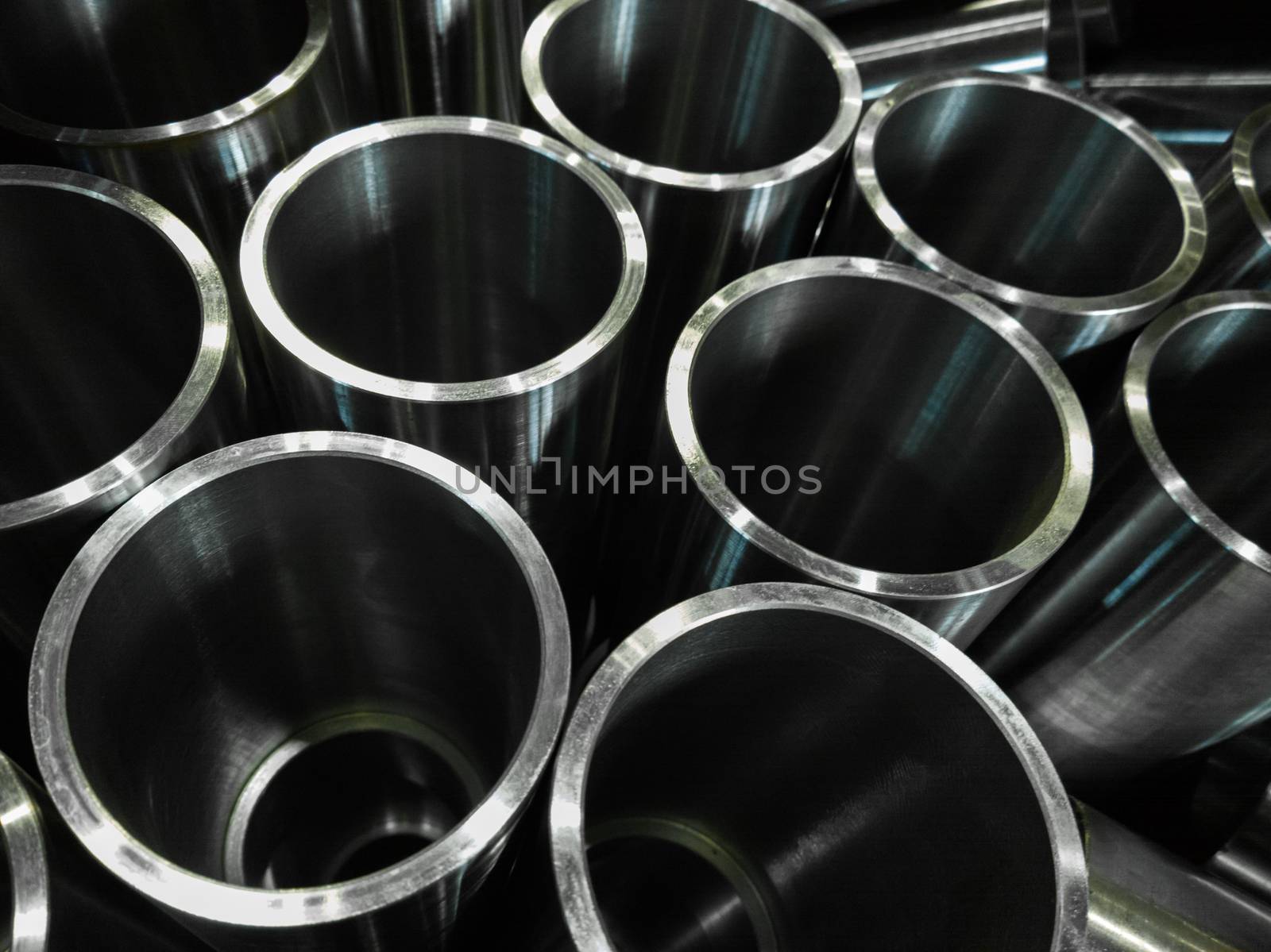 dark industrial background with cnc machined shiny steel pipes - selective focus and lens blur technique