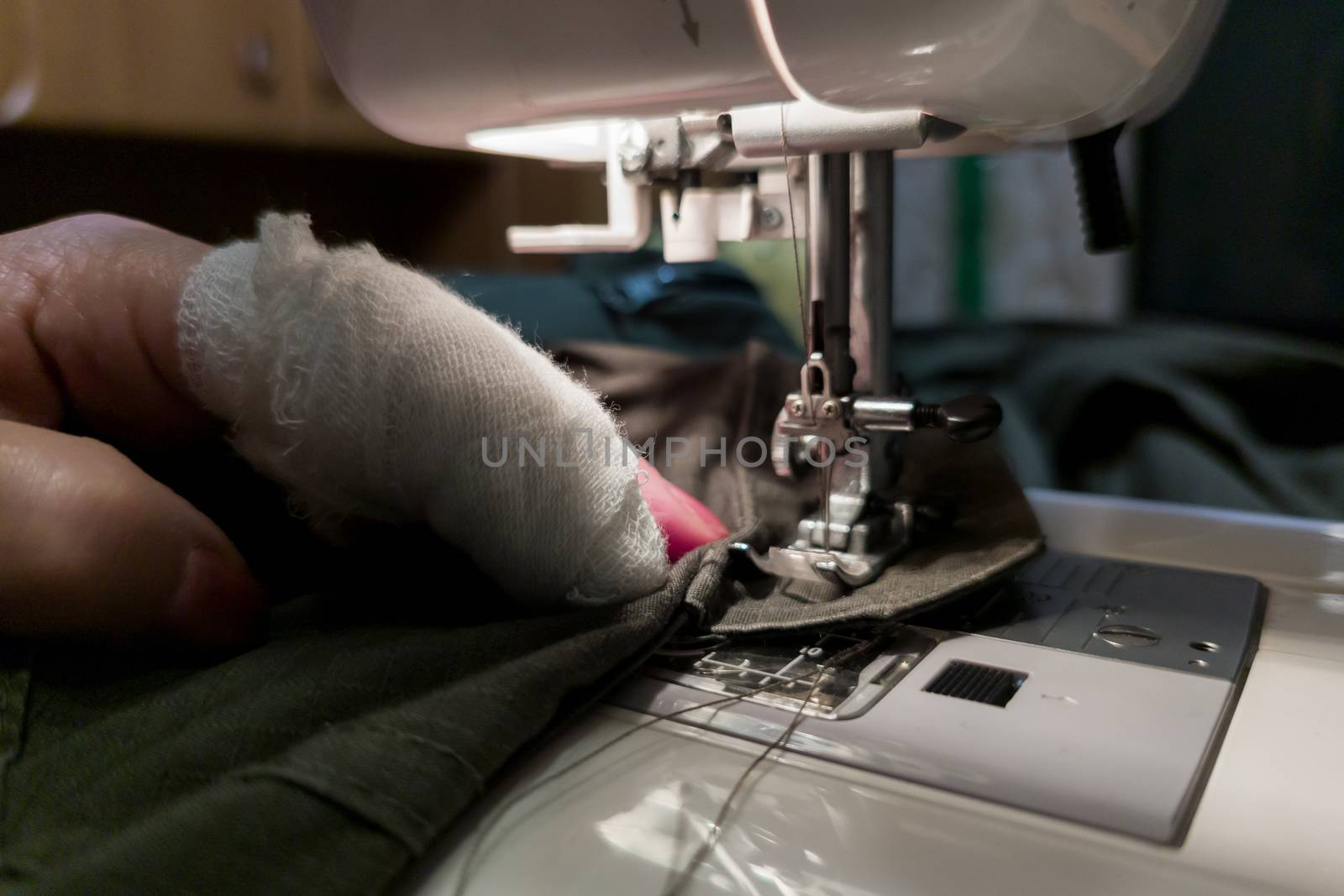 a hand of aged womans with a bandaged finger sews with a sewing machine - close-up with selective focus