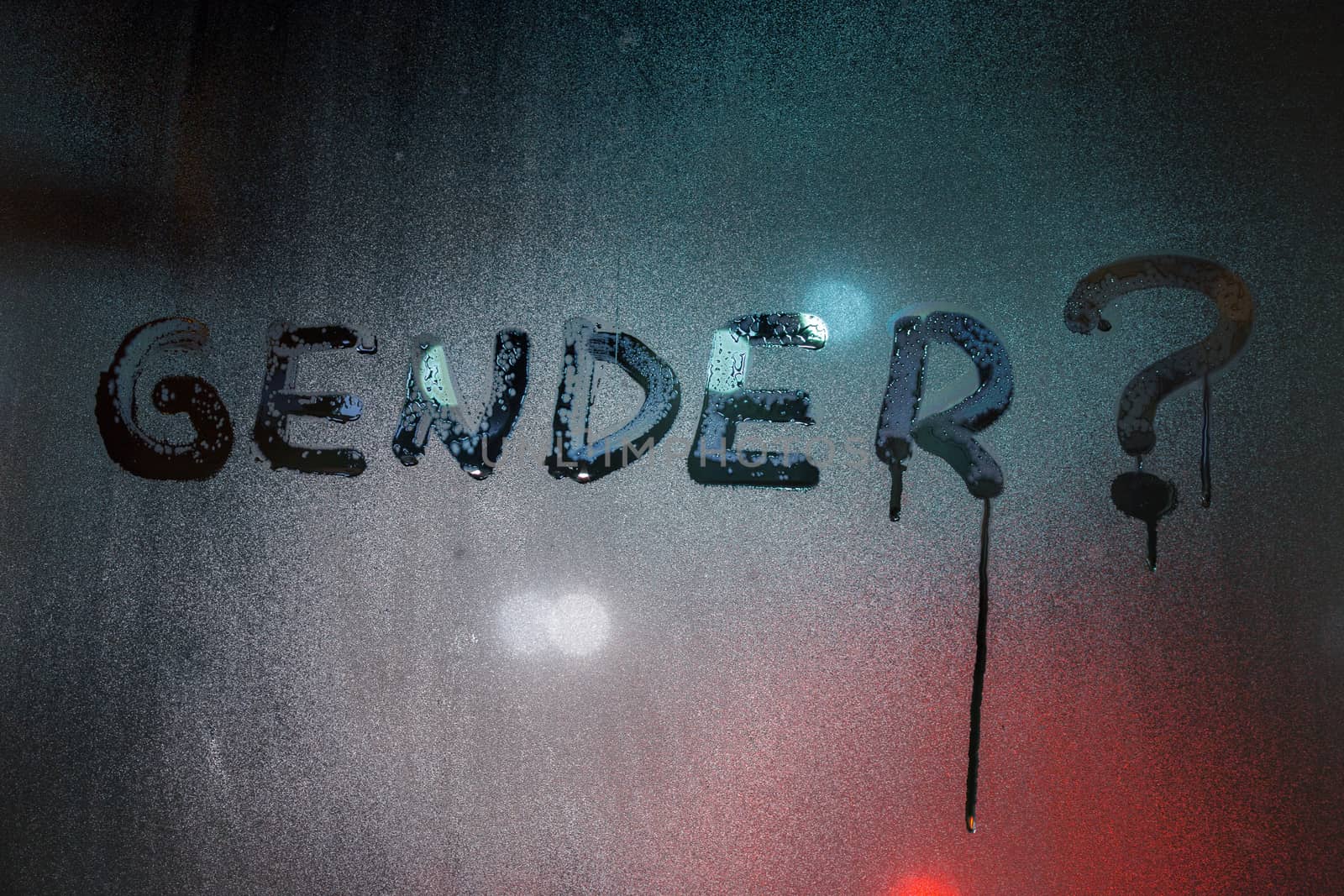 the question gender written by finger on night wet glass with blurred lights in background.