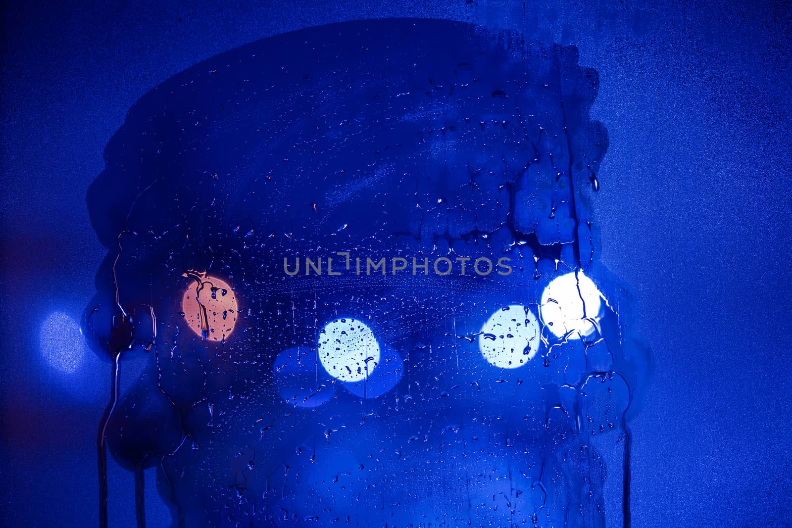an abstract background of blue tone night street lights bokeh trough half-wiped wet glass with selective focus.
