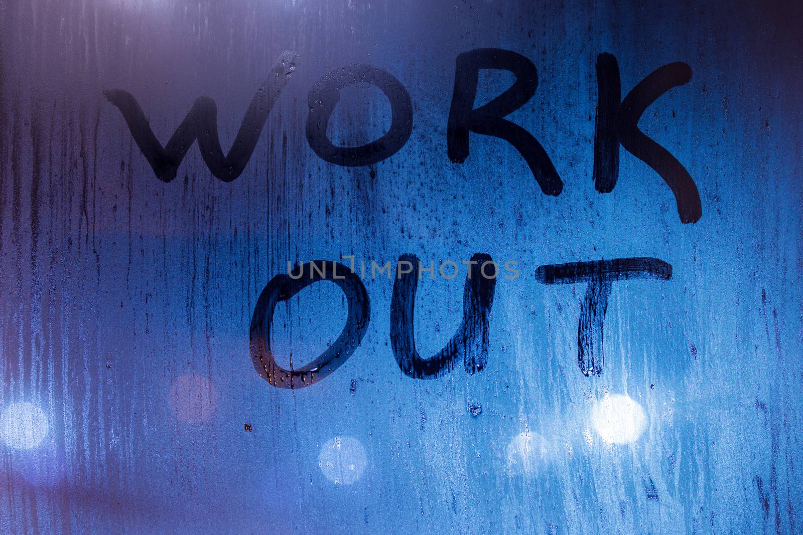 The word work out written on night sweaty window glass with blurred blue light in the background.