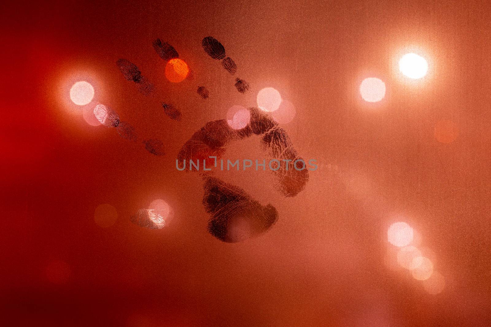 handprint on night wet glass in red colors with blurry street light in backround.