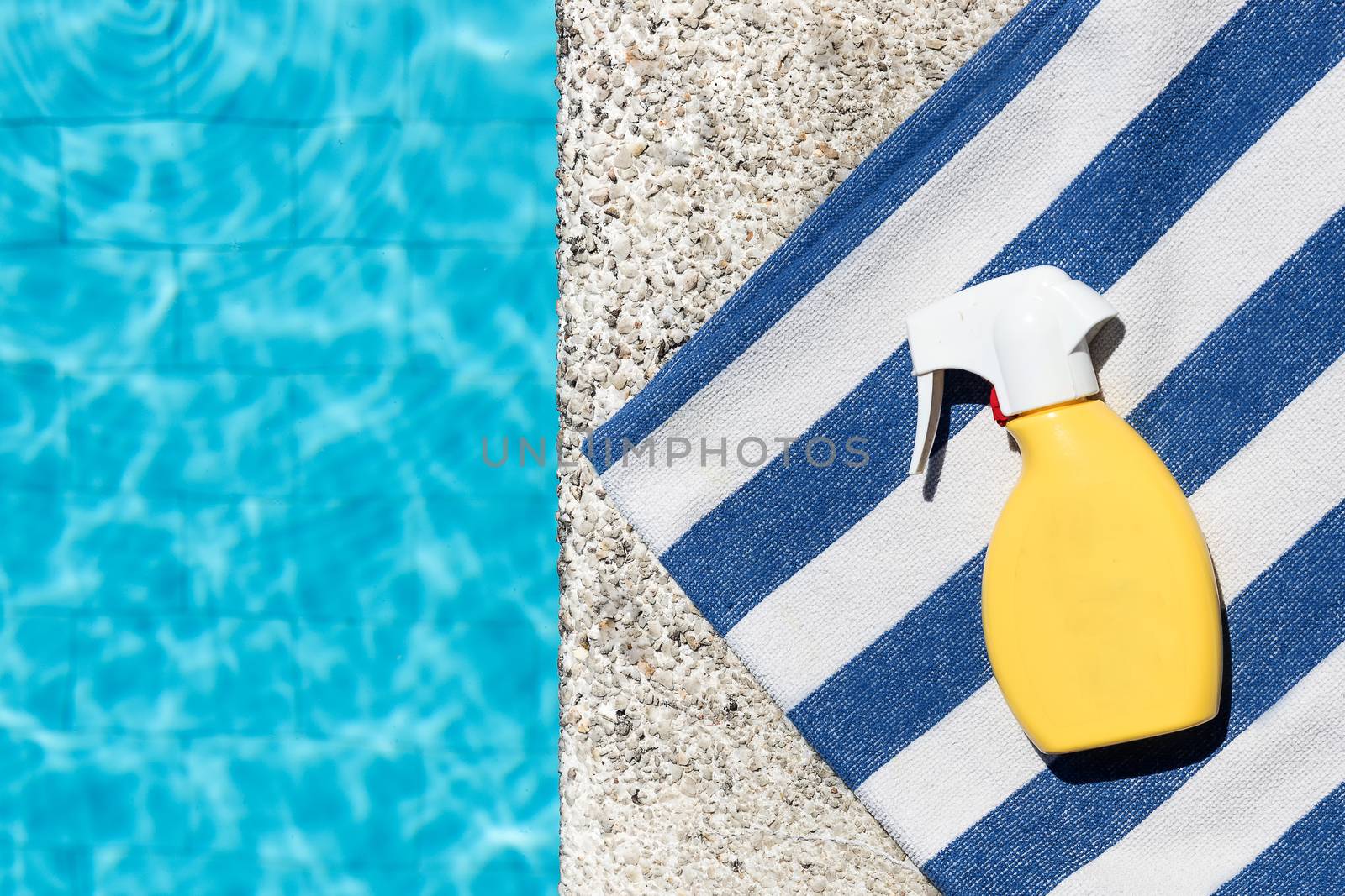 Sunscreen spray on a blue and white striped towel at the edge of a pool. Copy space. Top view.