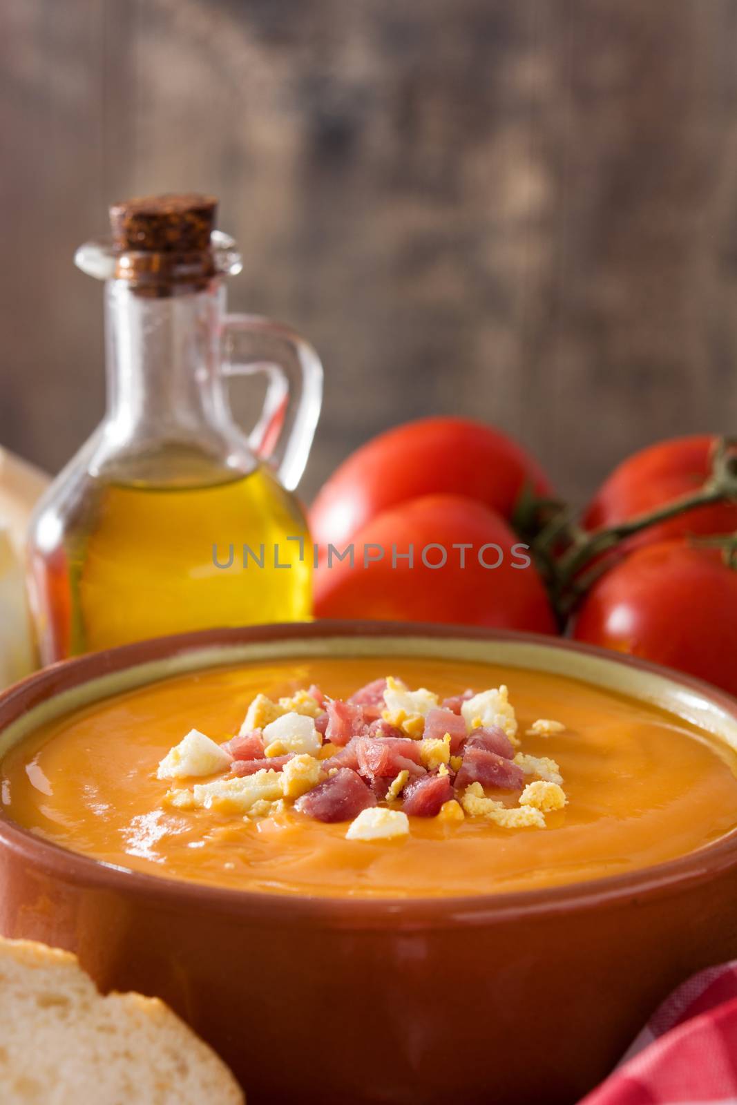 Typical Spanish salmorejo cream with ham and egg on wooden table.