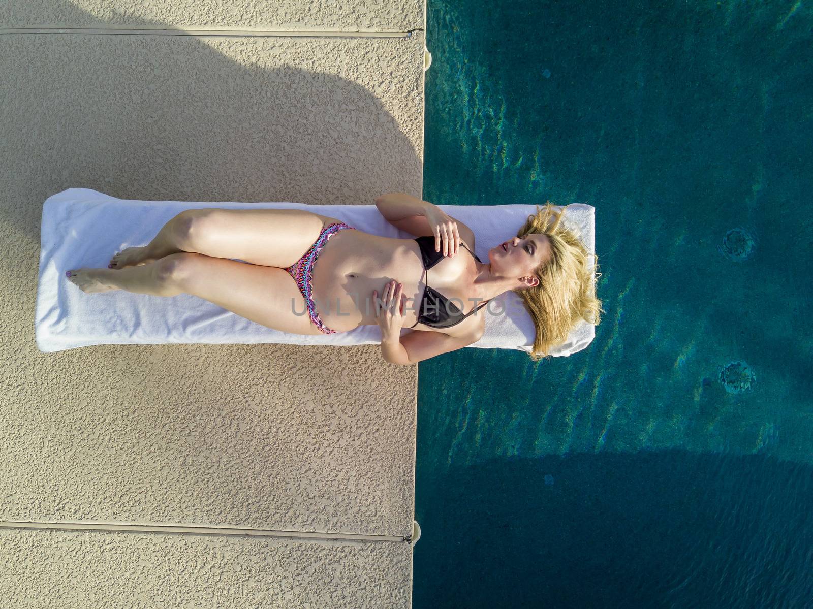 A blonde bikini model posing by a swimming pool