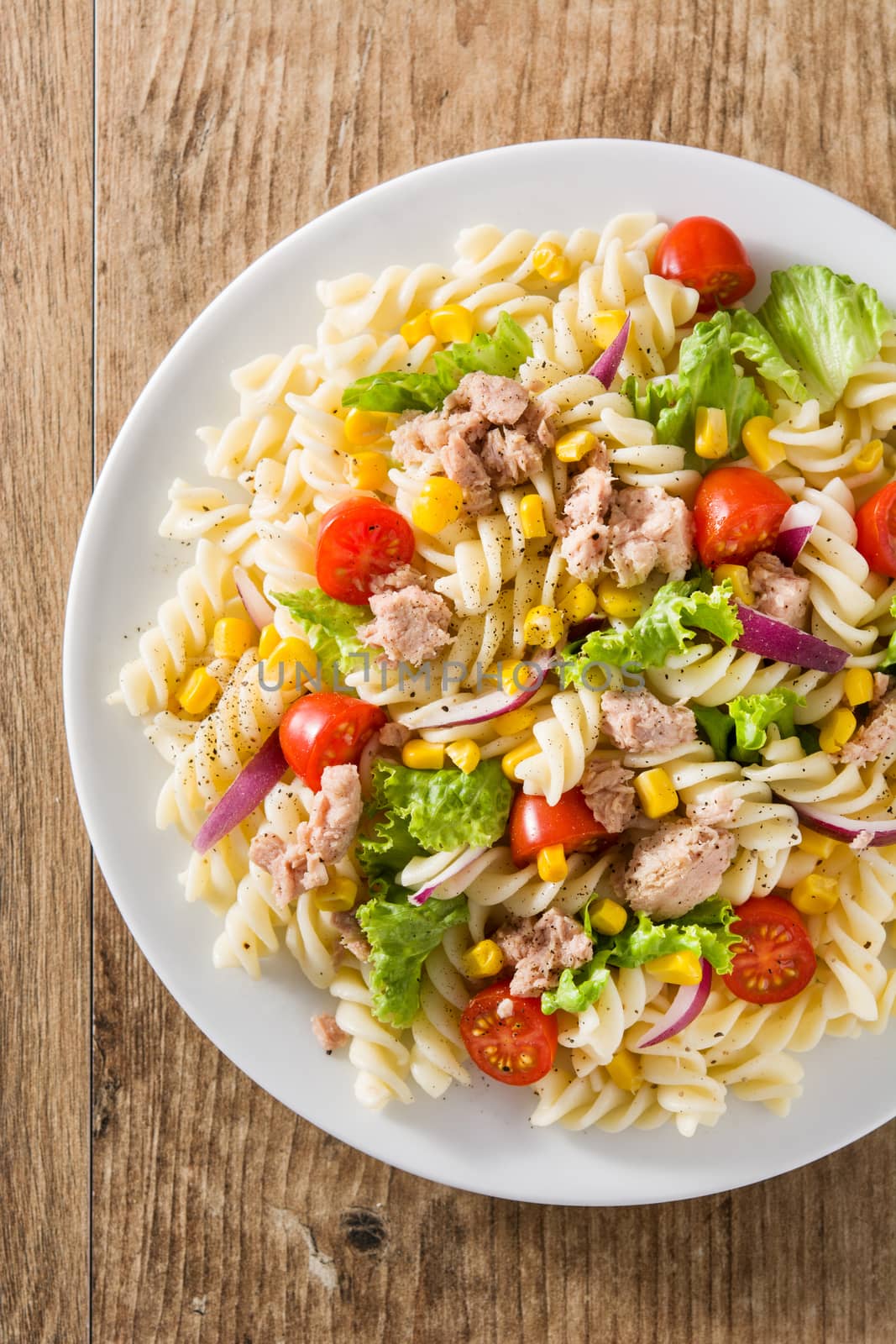 Pasta salad with vegetables in plate on wooden table by chandlervid85