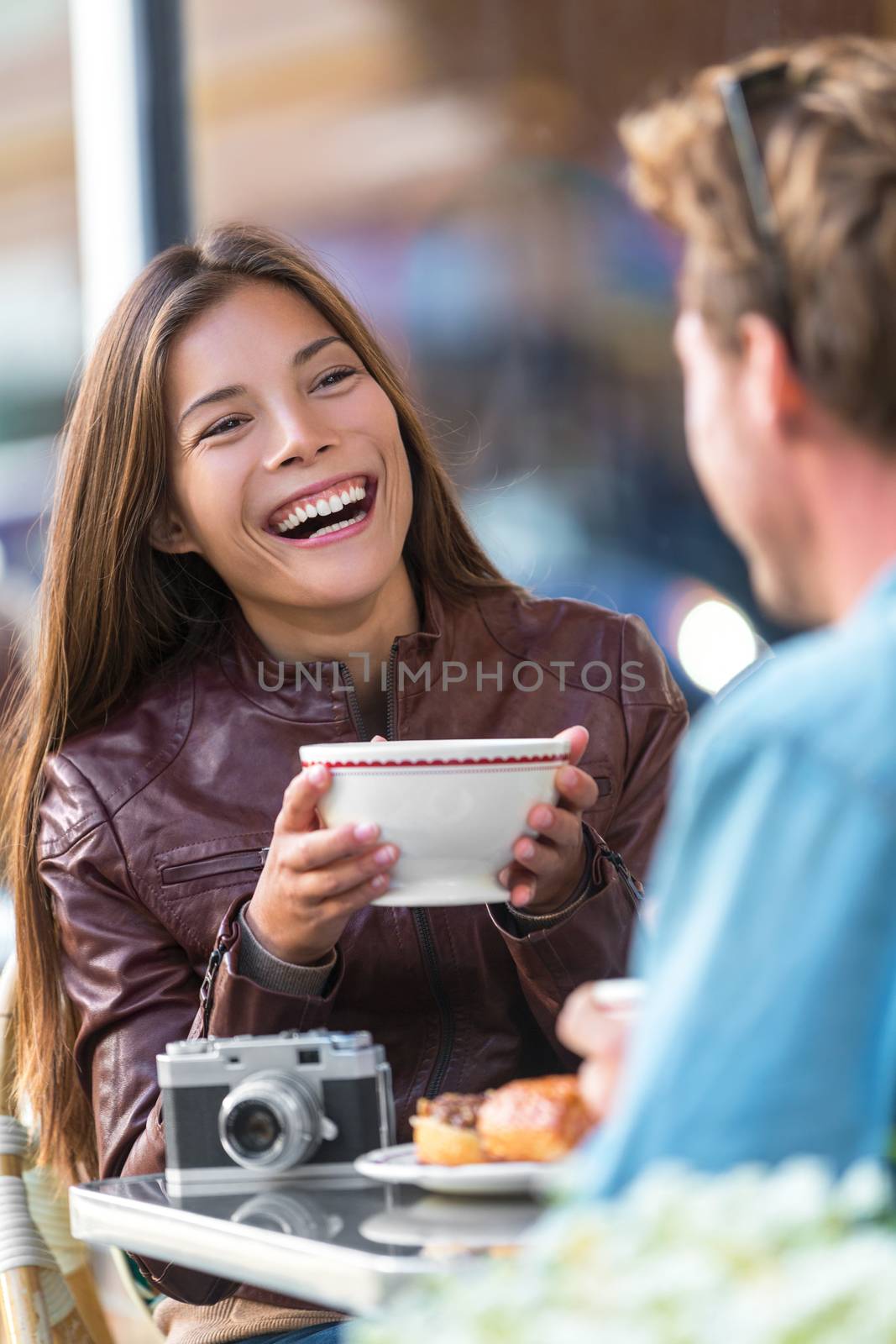 Happy woman drinking coffee at cafe. Asian girl, conversation with man friend laughing sitting at restaurant table having fun. Urban city couple lifestyle.