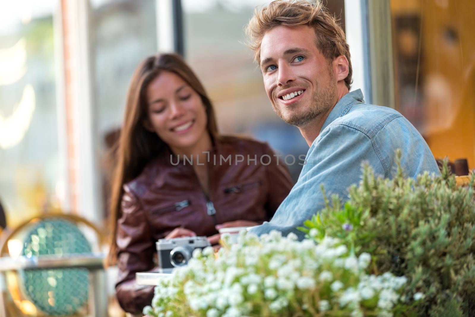 Young urban man enjoying sitting at restaurant table with friend in city. European travel couple vacation. Casual people lifestyle. by Maridav