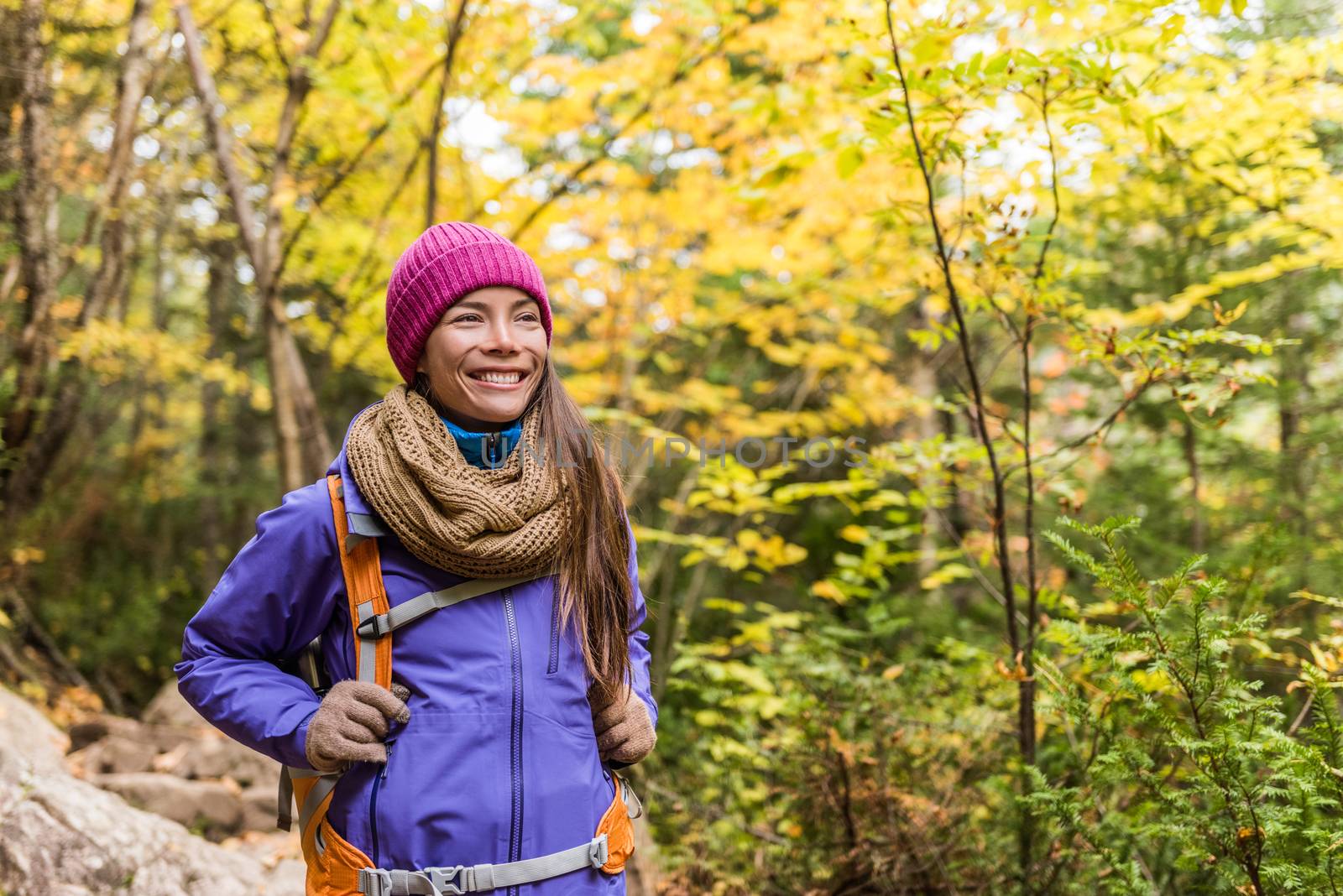 Happy asian woman hiking in autumn forest nature walking on trail path. Hiker girl with backpack, hat, scarf and jacket on fall adventure travel outdoors good weather during hike in cold weather. by Maridav