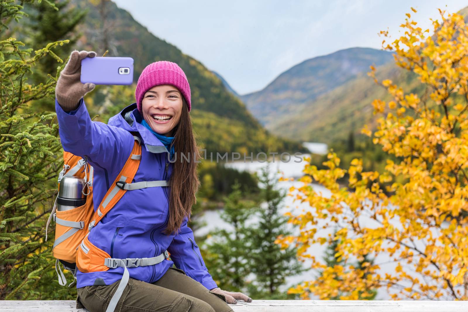 Happy asian hiker woman taking smartphone selfie at scenic viewpoint in nature fall mountain landscape outdoors. Girl hiking in Autumn forest park travel lifestyle. Girl holding phone. by Maridav
